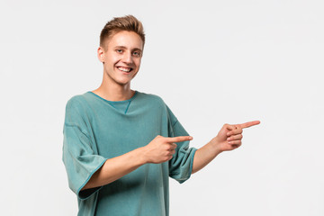 Handsome young man in a green tee showing with his fingers at the empty space for advertising in right side of white background.