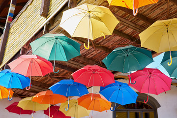 Fototapeta na wymiar Colorful umbrellas hang on the street under a wooden bridge.