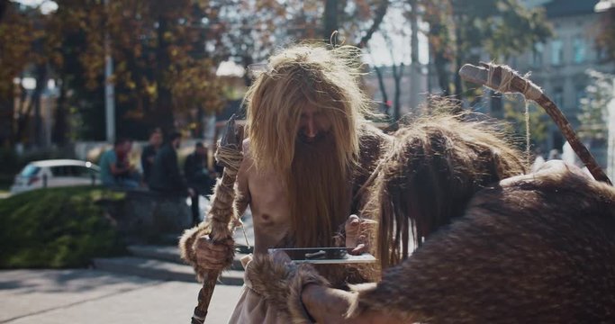 Funny caveman in animal fur using modern tablet browsing internet having fun civilization computer device evolution future homo sapiens humanity hunter-gatherers neanderthals paleolithic slow motion