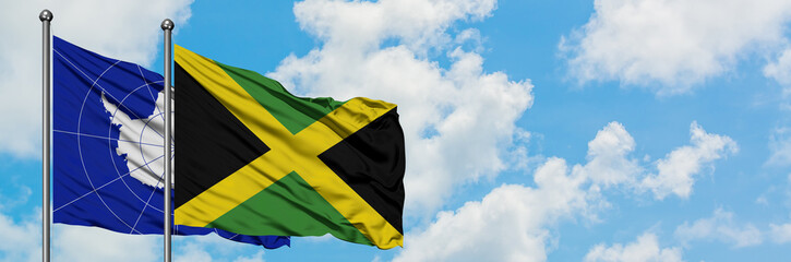 Antarctica and Jamaica flag waving in the wind against white cloudy blue sky together. Diplomacy concept, international relations.