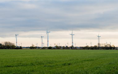 Wind turbines or windmills creating electricity from wind power on green field at sunset, Nordfriesland, Germany.
