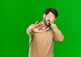 young businessman covering face with hand and putting other hand up front to stop camera, refusing...