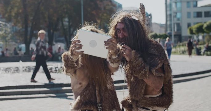 Caveman in animal fur using modern tablet take selfie browsing internet fun in modern city center caveman civilization computer evolution future homo sapiens human hunter-gatherers slow motion