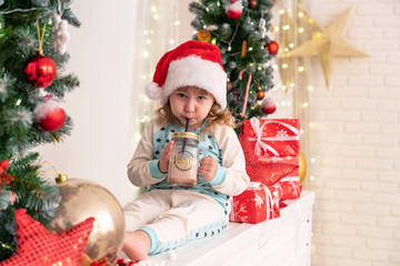 Fototapeta na wymiar little girl in pajamas and Santa hat drinking cocoa milk