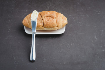 Croissant and a knife with butter on a dark stone table. Top view, copyspace. French breakfast