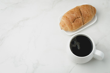 White mug with black coffee and croissant on white stone table. Top view and copyspace. Coffee break.