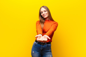 young pretty woman smiling happily with friendly, confident, positive look, offering and showing an...