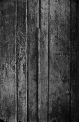 Weathered and aged wooden door, wall or wood panelling in black and white with paint peeling off.