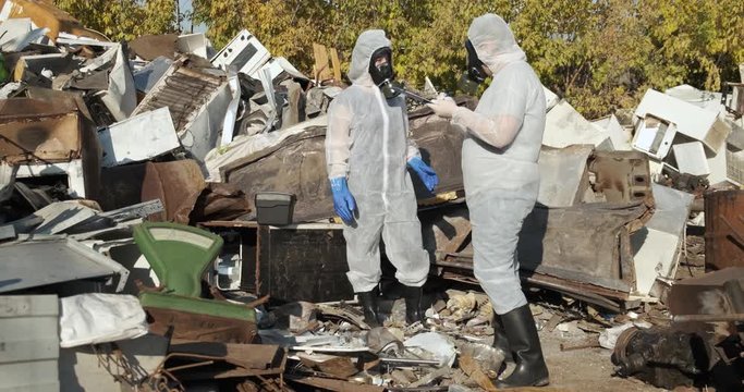Two scientists in protective suits are arguing with each other, it is impossible to breathe without respirator, yellowed trees, effect of poison on nature, very dangerous work, effects of chemicals