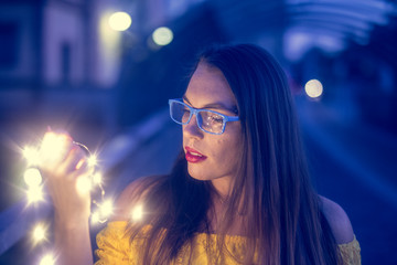 Junge Frau mit blauer Brille schaut in eine Lichterkette
