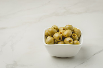 Green olives in a white ceramic bowl on a white background. Copyspace. Olives background