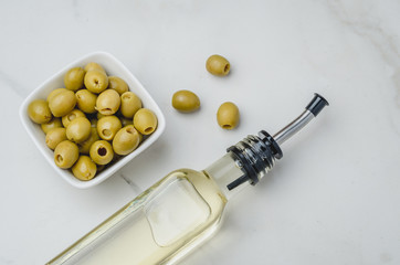 Glass bottle of olive oil and olive in a white bowl on a white stone background. Top view. Organic olive oil concept