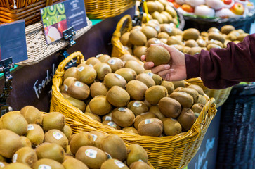 Women hand pick up kiwi in supermarket.