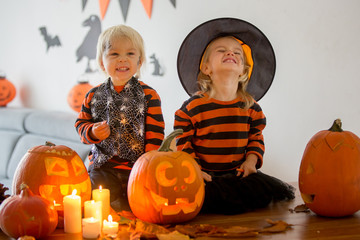 Adorable children, toddler boy and girl, playing with Halloween carved pumpking and decoration at home