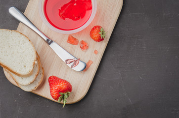 Strawberry jam. Bread and strawberry jam on a dark stone background with jar of jam and fresh strawberry. Top view, copyspace. Making sandwiches with strawberry jam.