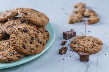 Stacked traditional chocolate chip cookies with pieces of cocoa on a green plate. Front view.