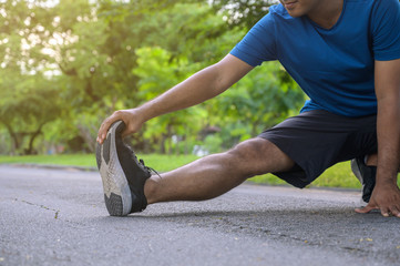 Young asian man stretching legs before run in park.