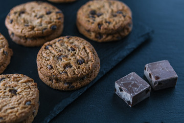 Handmade chocolate chip cookies and cocoa pieces on a chalkboard table.