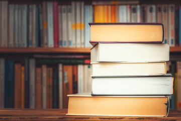 Pile of big books with blurry bookshelf in the background and copy space. Knowledge, reading, study, literacy or literature illustrative concept.