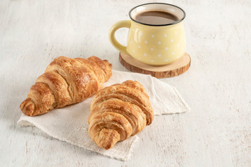 Crispy croissant and cup of coffee on a wooden table