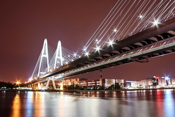 big cable-stayed bridge over the river at night with colorful bright lighting