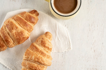 Crispy croissant and cup of coffee on a wooden table