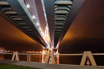 big cable-stayed bridge over the river at night with colorful bright lighting