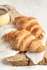 Crispy croissant and cup of coffee on a wooden table