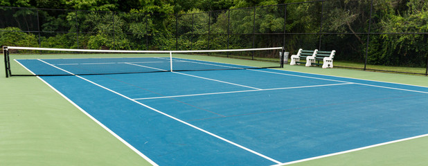 Sie view of blue tennis court with green boarder and benches to rest on - obrazy, fototapety, plakaty
