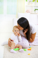  Young mom kissing her baby, sitting on the floor, playing with baby toys        
