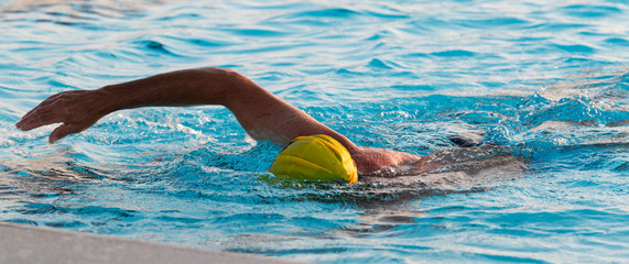 Man swimming in outdoor pool with yellow bathing cap