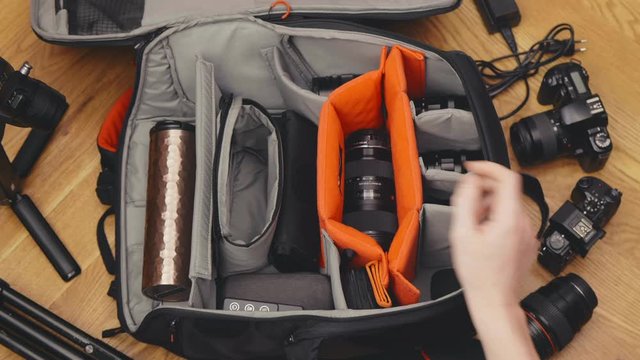 Photographer puts cameras, lens, flash in a bag before going on vacation
