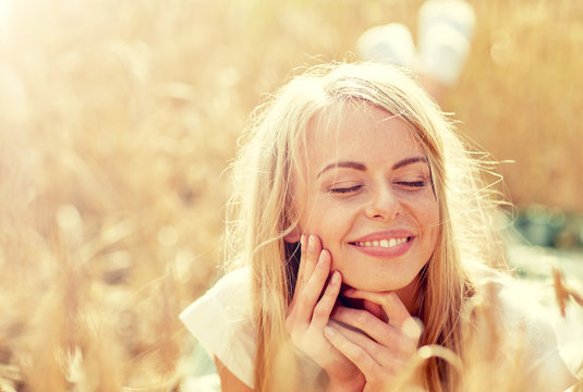 nature, summer holidays, vacation and people concept - happy smiling woman or teenage girl lying cereal field