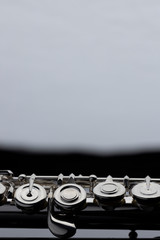 A silver plated flute on a dark reflective surface with a white background in the distance.