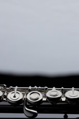 A silver plated flute on a dark reflective surface with a white background in the distance. © Janisphoto
