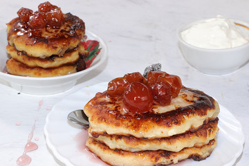 Cheesecake cottage cheese pancakes with sweet cherry jam on a light table close-up, delicious healthy dessert for breakfast. Healthy eating concept,