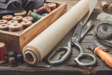 Sewing items: retro tailoring scissors, measuring tape, thimble, vintage spools of thread in wooden...