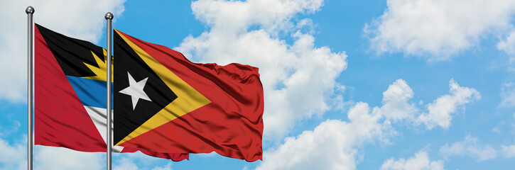 Naklejka premium Antigua and Barbuda with East Timor flag waving in the wind against white cloudy blue sky together. Diplomacy concept, international relations.