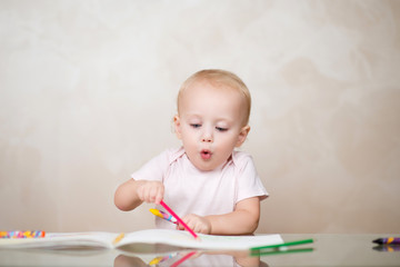 little girl with a funny facial expression enthusiastically draws with colored pencils in an album