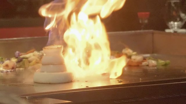 Chef fires up flambe on Teppanyaki hot plate in a restaurant, Slow motion