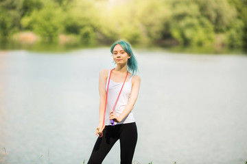 portrait of a beautiful young woman with green hair in a park near a lake with a skipping rope