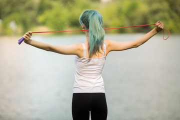 portrait of a beautiful young woman with green hair in a park near a lake with a skipping rope