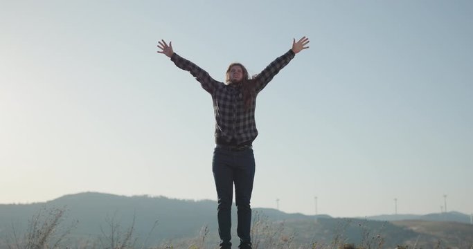 Successful man with arms up celebrating his victory. Celebrating success. Excited young man keeping arms raised and expressing positivity while stands on the mountain top