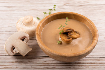 creamy mushroom soup in wooden bowl with roasted mushrooms and herbs on wooden table