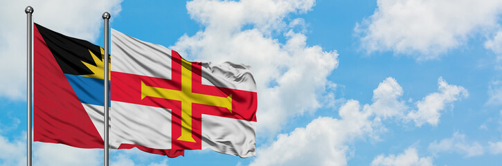 Antigua and Barbuda with Guernsey flag waving in the wind against white cloudy blue sky together. Diplomacy concept, international relations.