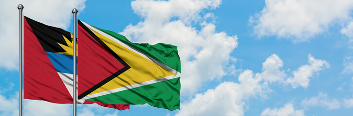 Antigua and Barbuda with Guyana flag waving in the wind against white cloudy blue sky together. Diplomacy concept, international relations.