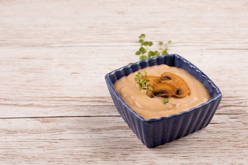 creamy mushroom soup in blue bowl with roasted mushrooms and herbs on wooden table