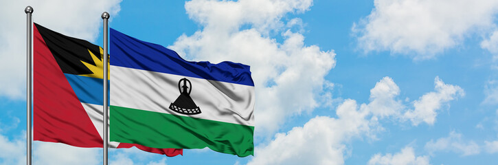 Antigua and Barbuda with Lesotho flag waving in the wind against white cloudy blue sky together....