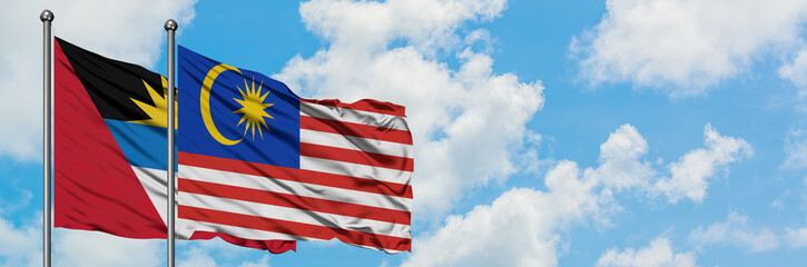 Antigua and Barbuda with Malaysia flag waving in the wind against white cloudy blue sky together. Diplomacy concept, international relations.