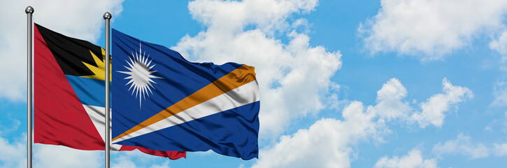Antigua and Barbuda with Marshall Islands flag waving in the wind against white cloudy blue sky together. Diplomacy concept, international relations.